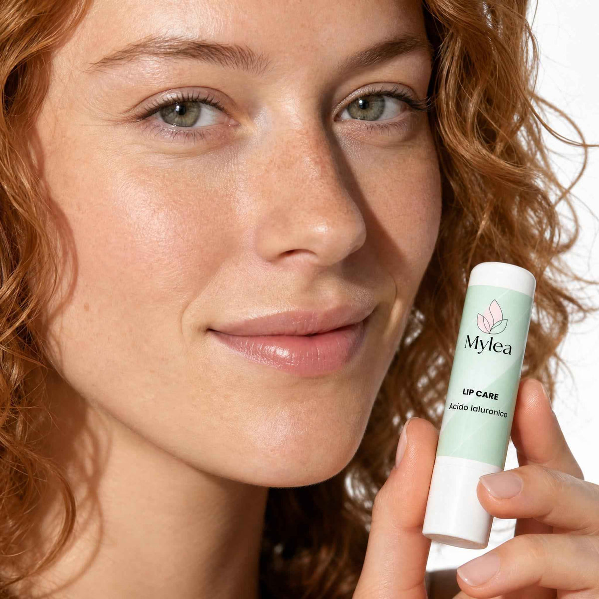 Modella con capelli rossi che tiene in mano il balsamo labbra idratante Mylea Lip Care con acido ialuronico
