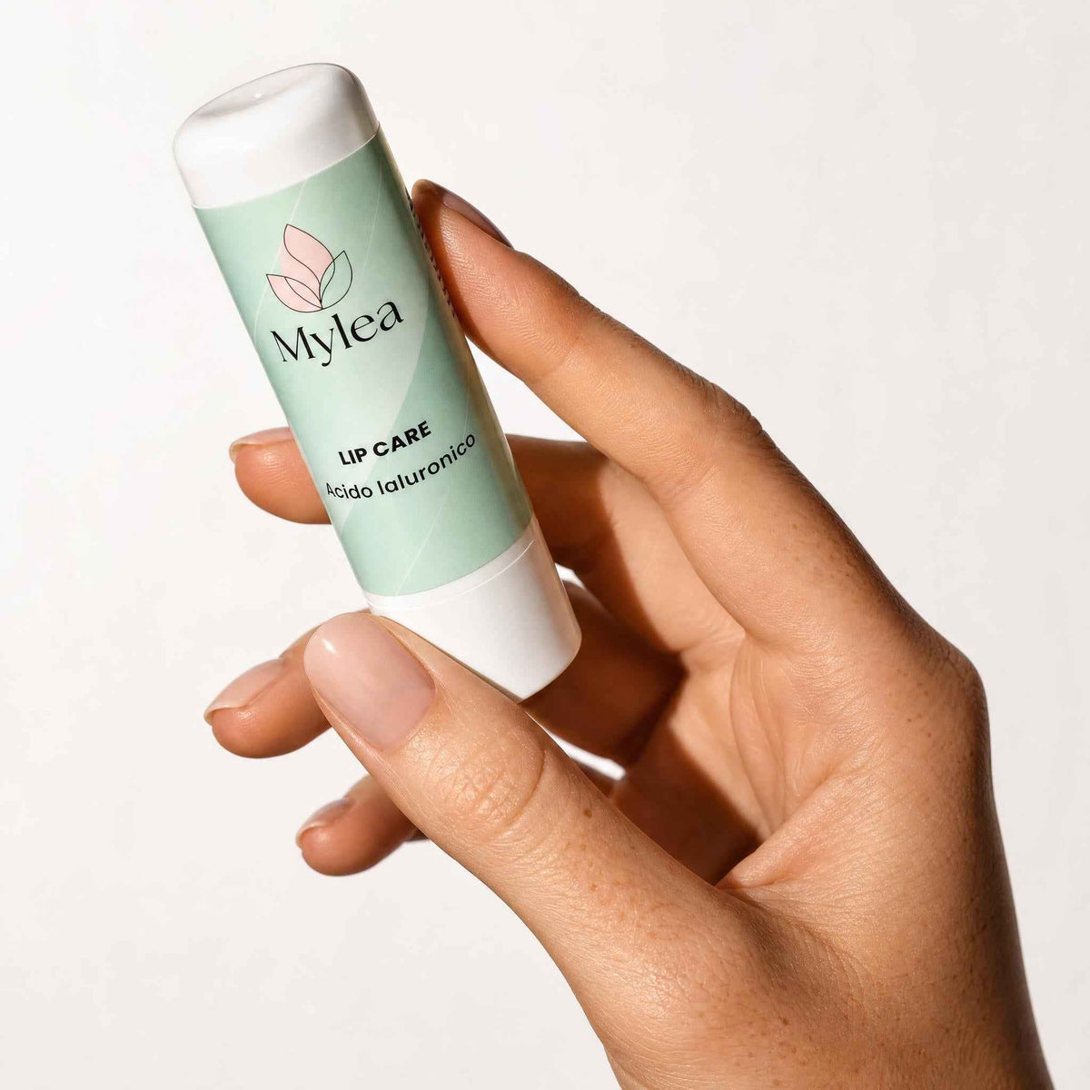 Mano che tiene il balsamo labbra idratante Mylea Lip Care con acido ialuronico in stick verde chiaro